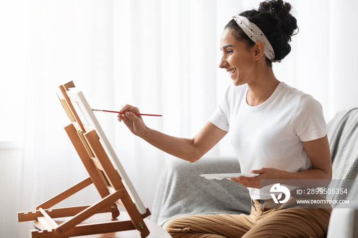 Inspired brunette woman sitting on couch and painting