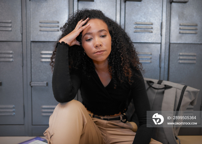 A young mixed race woman sits in front of school lockers looking depressed