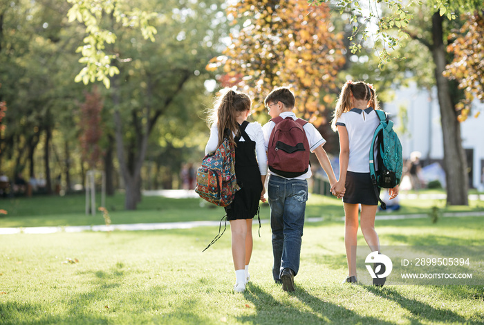 school friends a boy and two girls with school backpacks on their backs walk after class