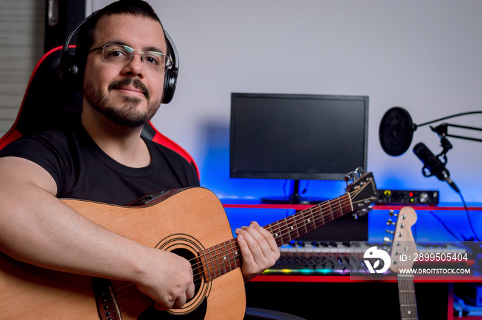 portrait happy latino young man sitting in his music studio with his acoustic guitar