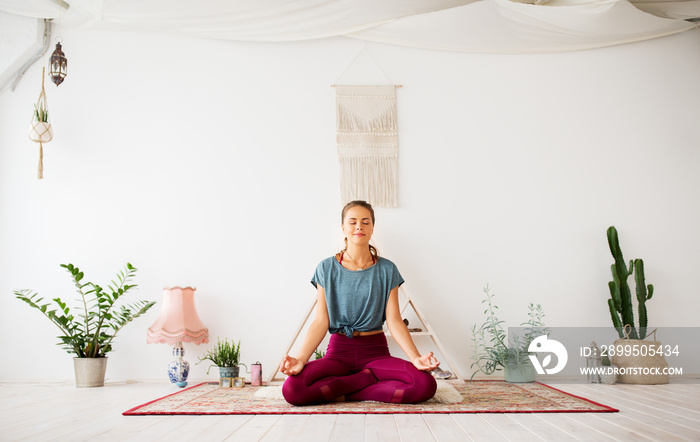 mindfulness, spirituality and healthy lifestyle concept - woman meditating in lotus pose at yoga studio