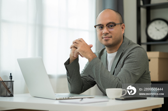 A man around the age of 35. Working at home by meeting video conference looking at camera. He was wearing a grey suit and glasses. Asian businessman work from home talking on screen.