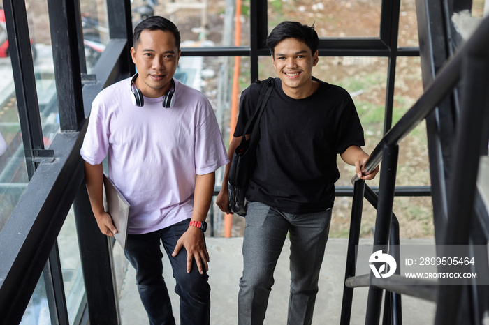 Two asian college students smilling to camera while climbing up the stairs