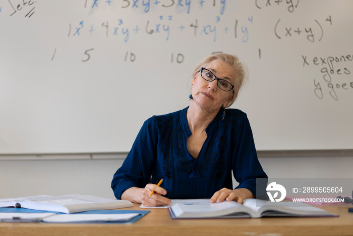 Portrait of frustrated tired high school math teacher sitting on desk talking to students.