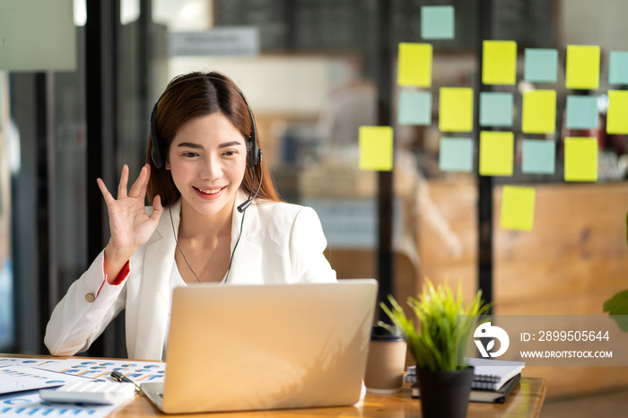 Confident young businesswoman wearing headphones and discussing project details with clients on video call. Skilled woman worker with headphones conducting online meeting with colleagues