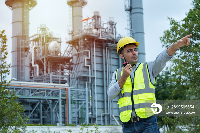 worker talking on the radio communication. industrial engineer in Oil factory. Engineer wearing PPE uniform and helmet looking detail tablet on hand with power plant  on background.