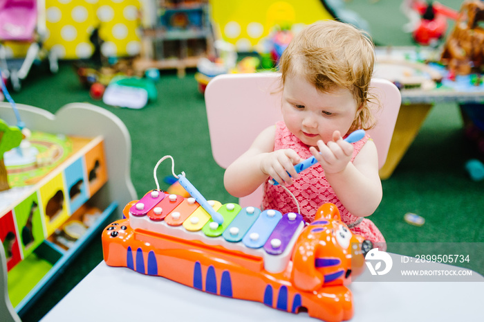 Kid, child, baby girl one year, plays a musical instrument xylophone in children’s room for birthday or home. Game center.