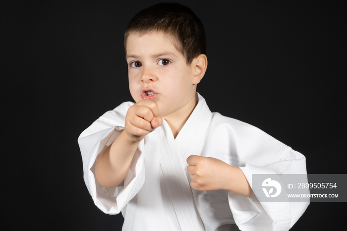 A little boy practices martial arts, karate classes in kimono on a black background, a place for text