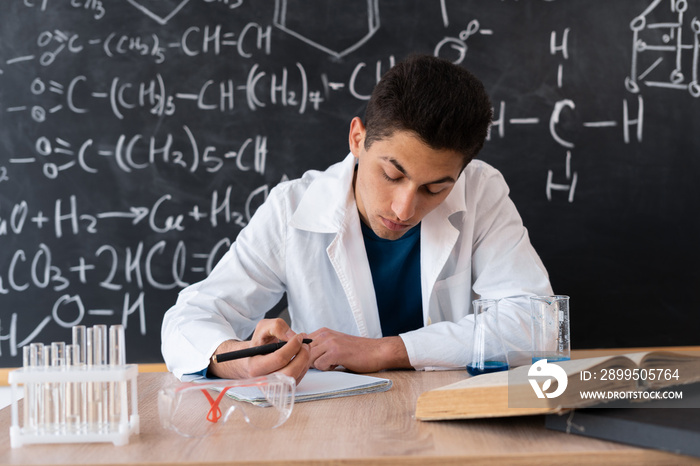 A young scientist chemist at the university is preparing for an exam, studying chemistry as a science at school, Arabic student at a chemistry lesson, blackboard background with chemical formulas