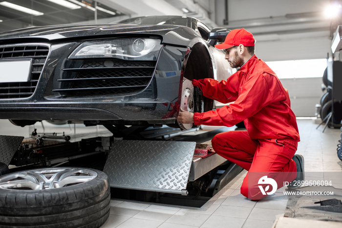 Auto mechanic in red uniform servicing sports car checking front brakes in the car service