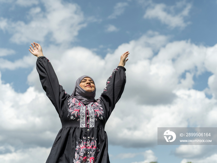 UK,Sutton,Woman in traditional dress and headscarf with arms raised