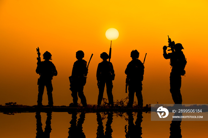 The military silhouettes of soldiers hold gun against with sunset sky background.