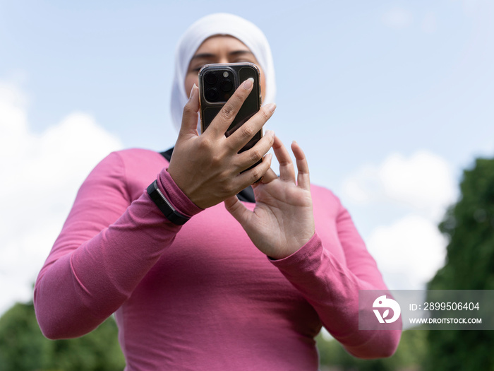 UK,Sutton,Low angle view of woman in headscarf holding smart phone in park