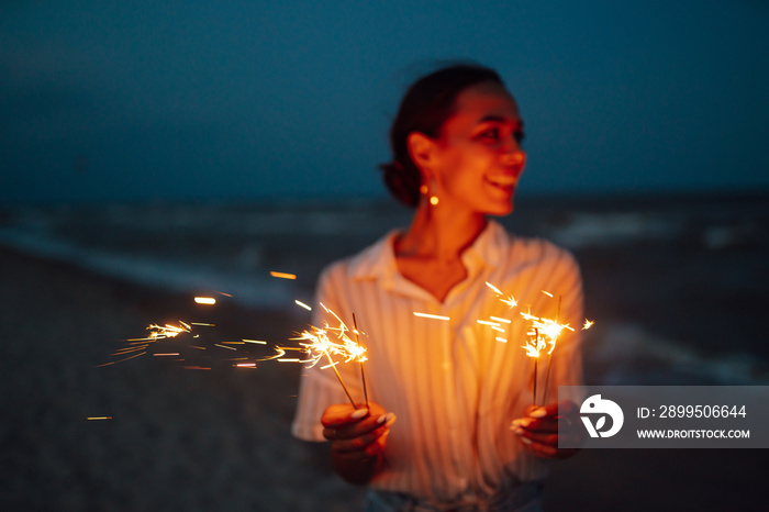 Glowing sparkles in hands. Women with Christmas sparklers on nature and twillight sky background. Holidays, vacation, relax and lifestyle concept.