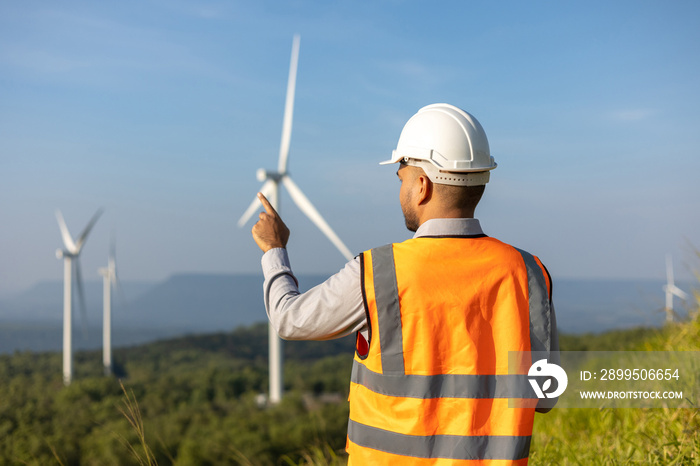 Engineer India man working with tablet at windmill farm Generating electricity clean energy. Wind turbine farm generator by alternative green energy. Asian engineer checking control electric power