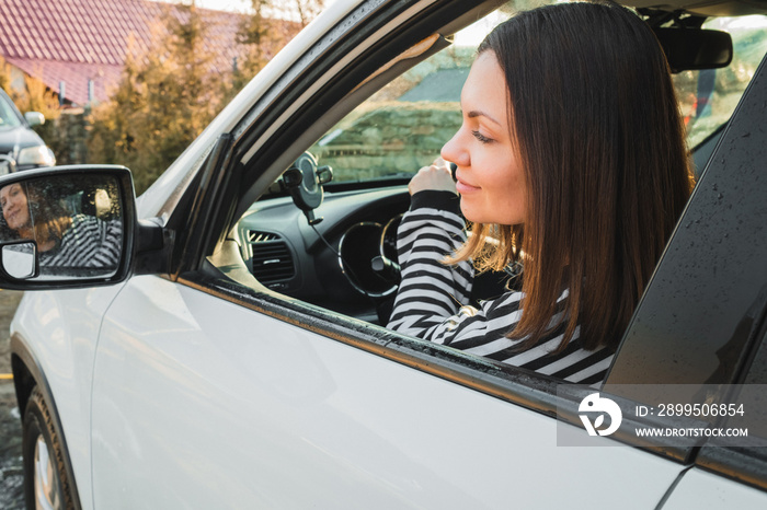 Happy woman driving white car, lady smiling, looking to mirror. Successful girl in automobile.