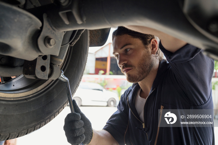 A car mechanic repairing the brakes and shock absorber. Car brake repairing in garage. Auto mechanic hands using wrench to repair a car engine.