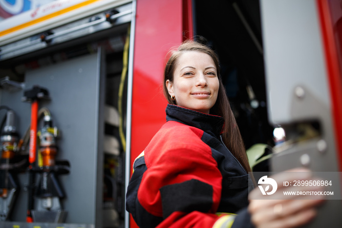 Photo of young fire woman with long hair looks at camera next to fire engine