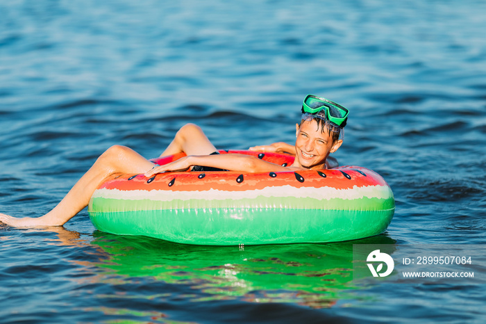 Happy boy in glasses for swimming on an inflatable circle swims in the sea. A little boy has fun and swims on an inflatable circle. Summer holiday