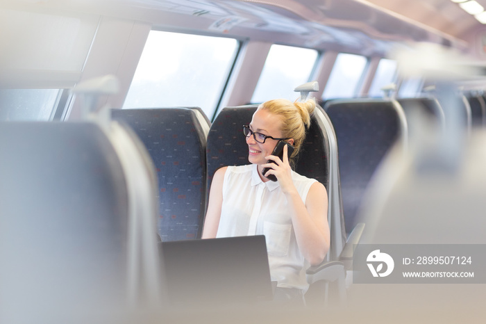 Businesswoman talking on cellphone and working on laptop while traveling by train. Business travel concept.