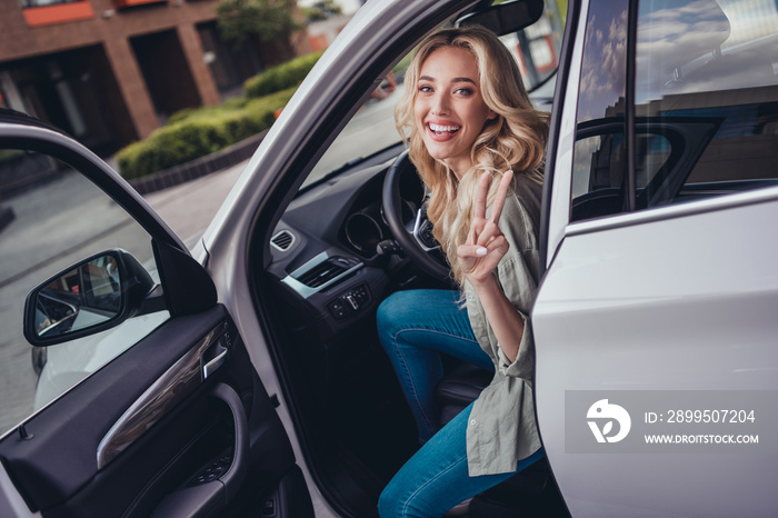 Photo of positive pretty girl sitting car seat hand fingers demonstrate v-sign street outdoors