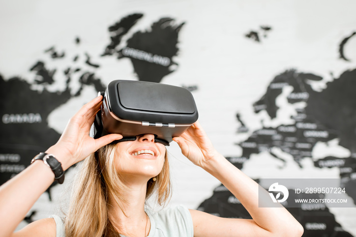 Young woman using virtual reality glasses sitting indoors with world map on the background