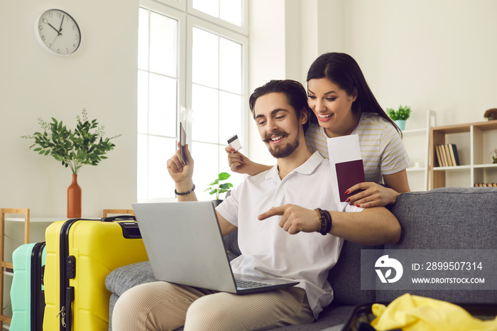 Happy married couple at home using a laptop to pay for tickets and book a hotel room online. Man and a woman with already collected suitcases are ready for vacation. Concept of summer vacation abroad.