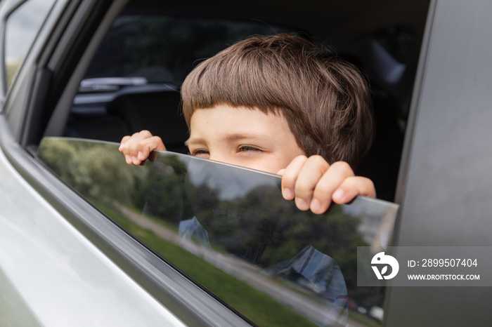 Cheerful little boy looks out the open window and enjoys ride with parents in car in summer, outdoor, free space