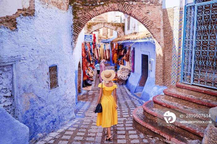 Colorful traveling by Morocco. Young woman in yellow dress walking in  medina of  blue city Chefchaouen.