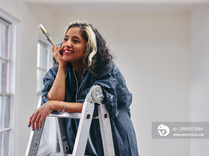 Smiling woman standing on ladder with paintbrush