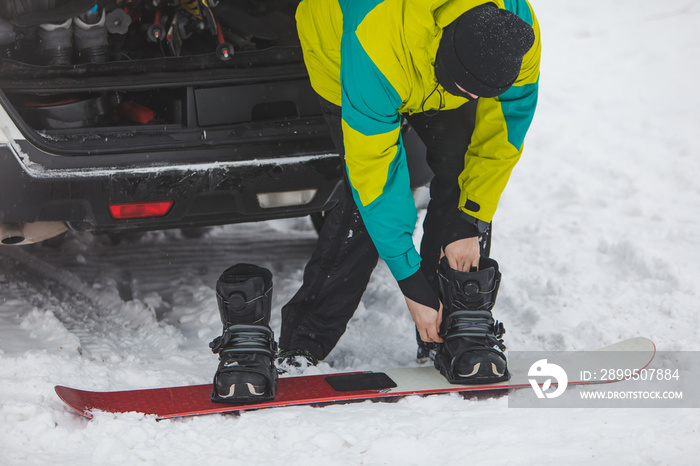 man changing regular boots to snowboard at parking place near car