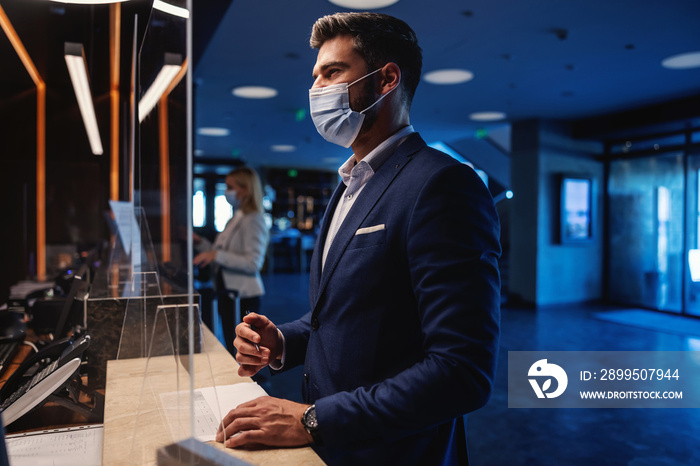 Businessman with face mask standing at reception and checking in to the hotel during coronavirus pandemic. Business trip, travel destinations, COVID-19 outbreak situation