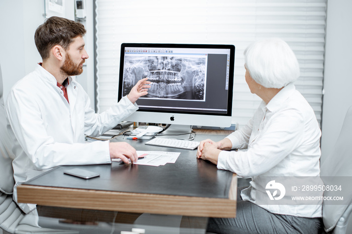 Senior woman patient during the medical consultation with dentist showing dental x-ray on the monitor