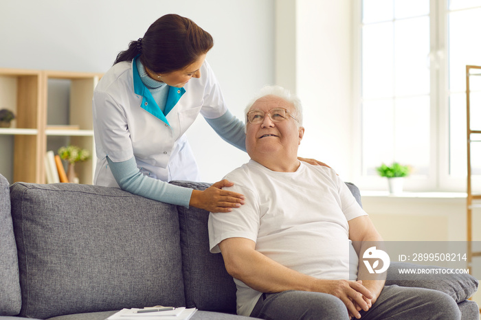 Friendly female doctor visits, supports and encourages her senior patient at home.