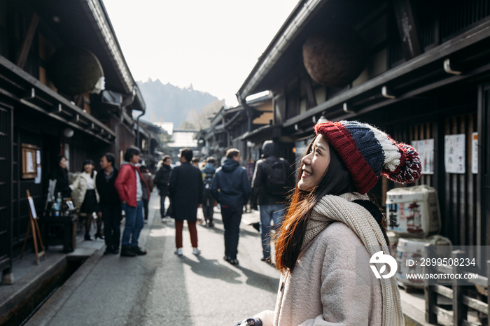 Asian cute girl standing with blur unidentify people in middle of Japanese old town with houses Edo style in Hida Takayama, Gifu, Japan.