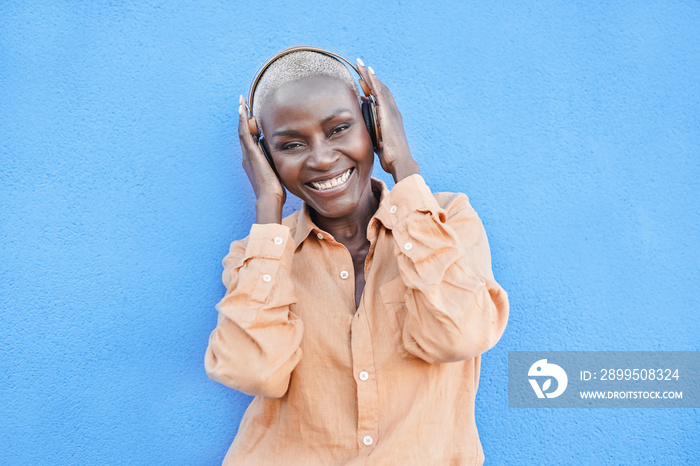 Mature african woman dancing to music playlist while holding wireless headphone - Black mature person enjoy technology