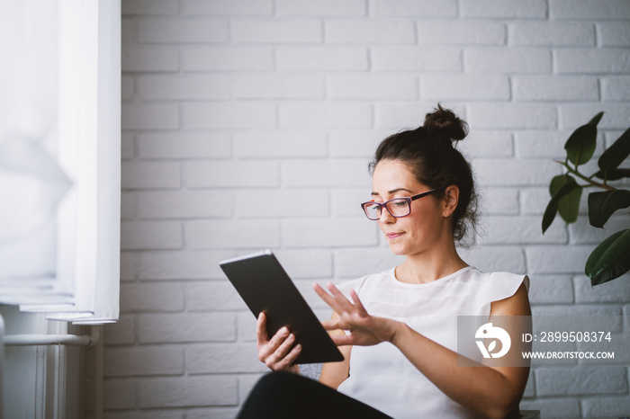 Middle aged attractive woman looking at tablet searching online.