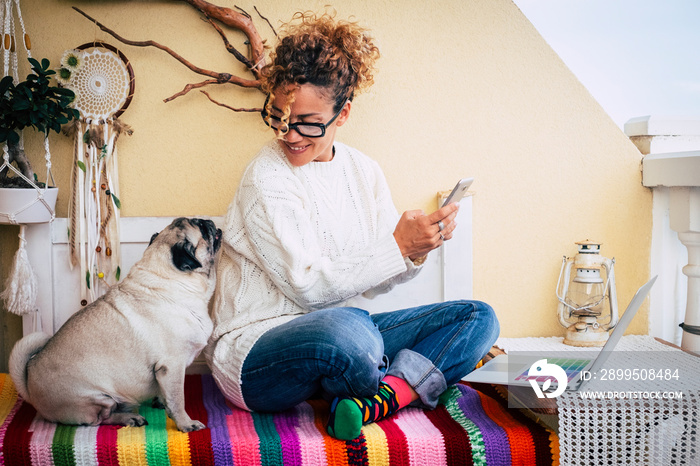 Happy couple people and animals with cheerful beautiful caucasian woman and her lovely pug dog sit down at home while work with technology devices like phone and laptop