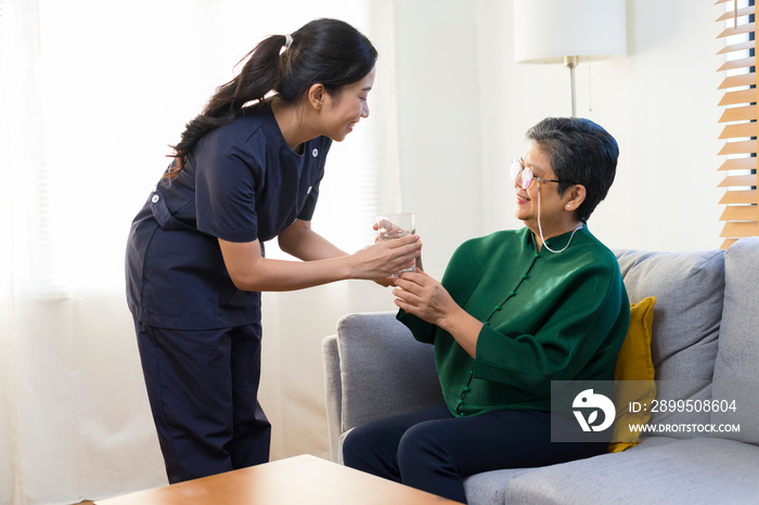 Smiling nurse giving glass of water to senior asian woman in nursing home or assisted living facility.