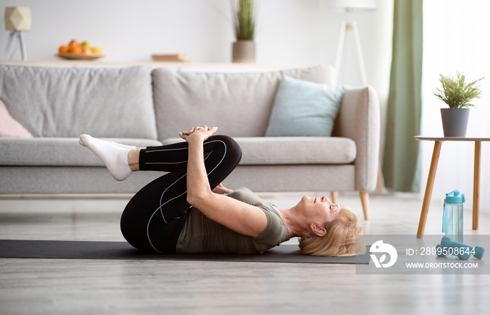 Sporty senior woman doing exercises on yoga mat indoors, blank space