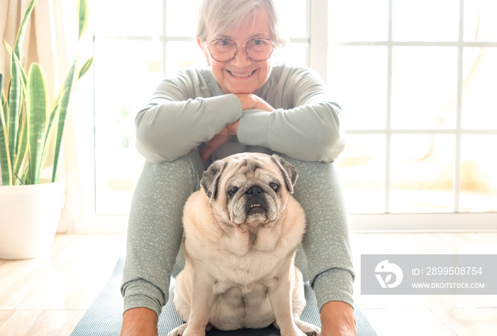 Close up portrait of old  pug dog looking at camera. Senior smiling woman sitting on floor ready to practice yoga exercises enjoying relax with her best friend. Dog therapy concept