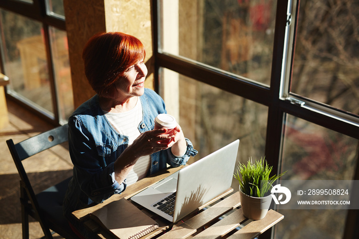 Serene woman with drink looking through window at sunset