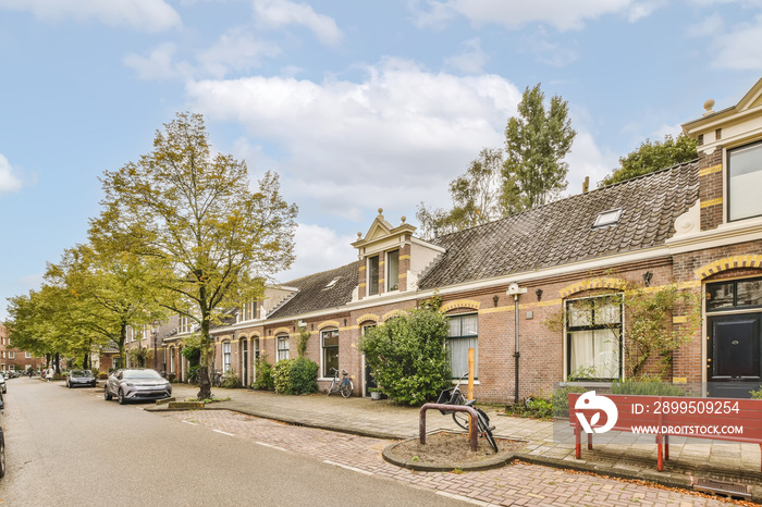 a street in the netherlands with houses on either sides and cars parked along the road there is a red bench