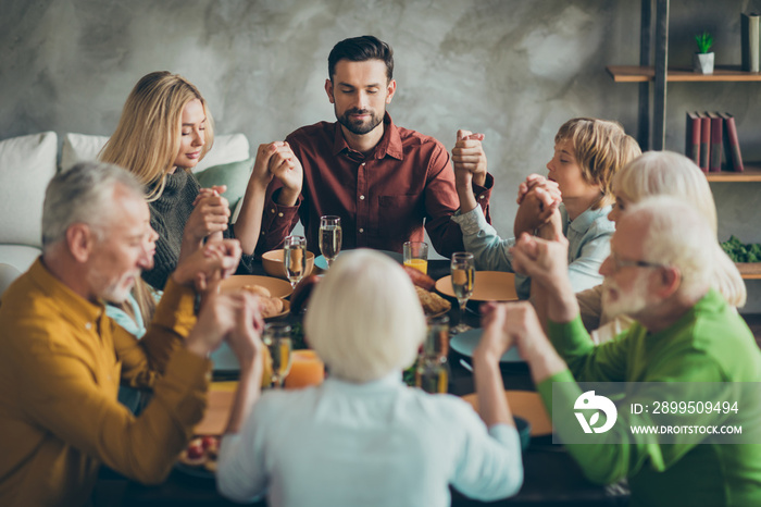 Big family father mother mature grandparents kids small girl boy gather sit table enjoy november feast meal pray celebrate thanksgiving day hold hands in house