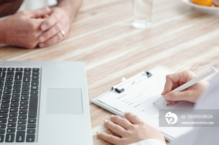 Hands of general practitioner filling medical form when talking to patient in medical office