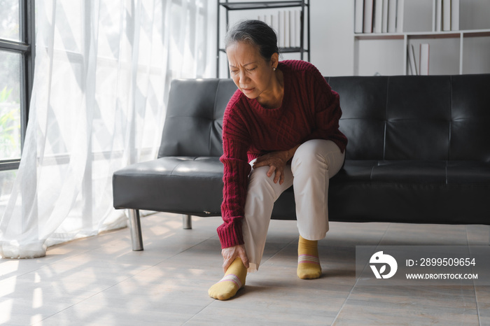 Elderly asian housewife woman sitting on sofa. heel pain or foot pain