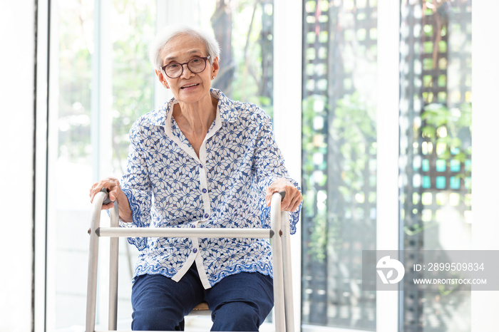 Asian senior woman sitting with walker during rehabilitation, elderly woman wear glasses,smiling and looking at camera in home