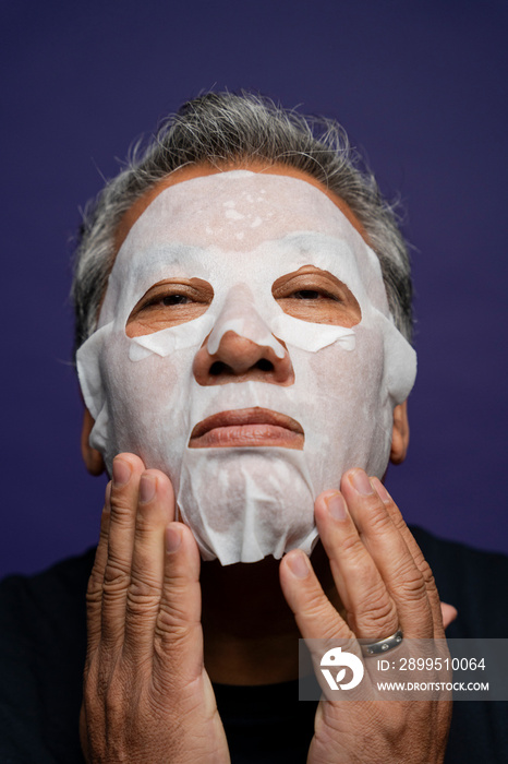 Portrait of man applying facial mask against purple background