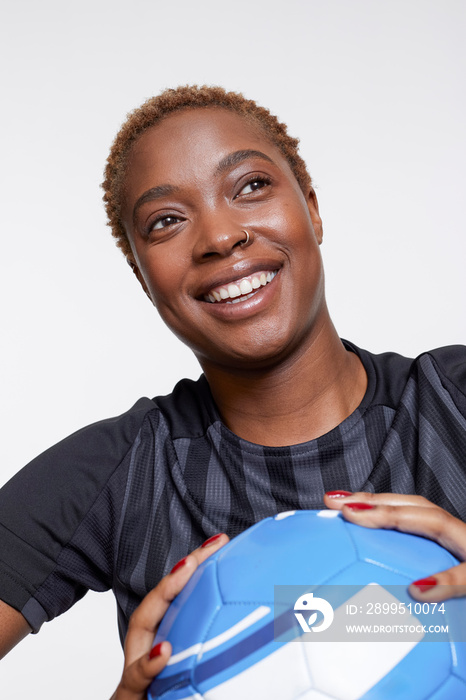 Studio portrait of smiling female soccer player with ball