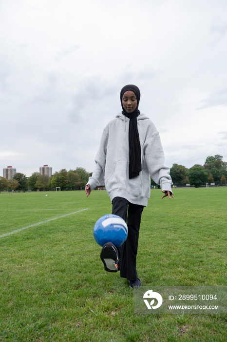 Woman in hijab kicking soccer ball in park